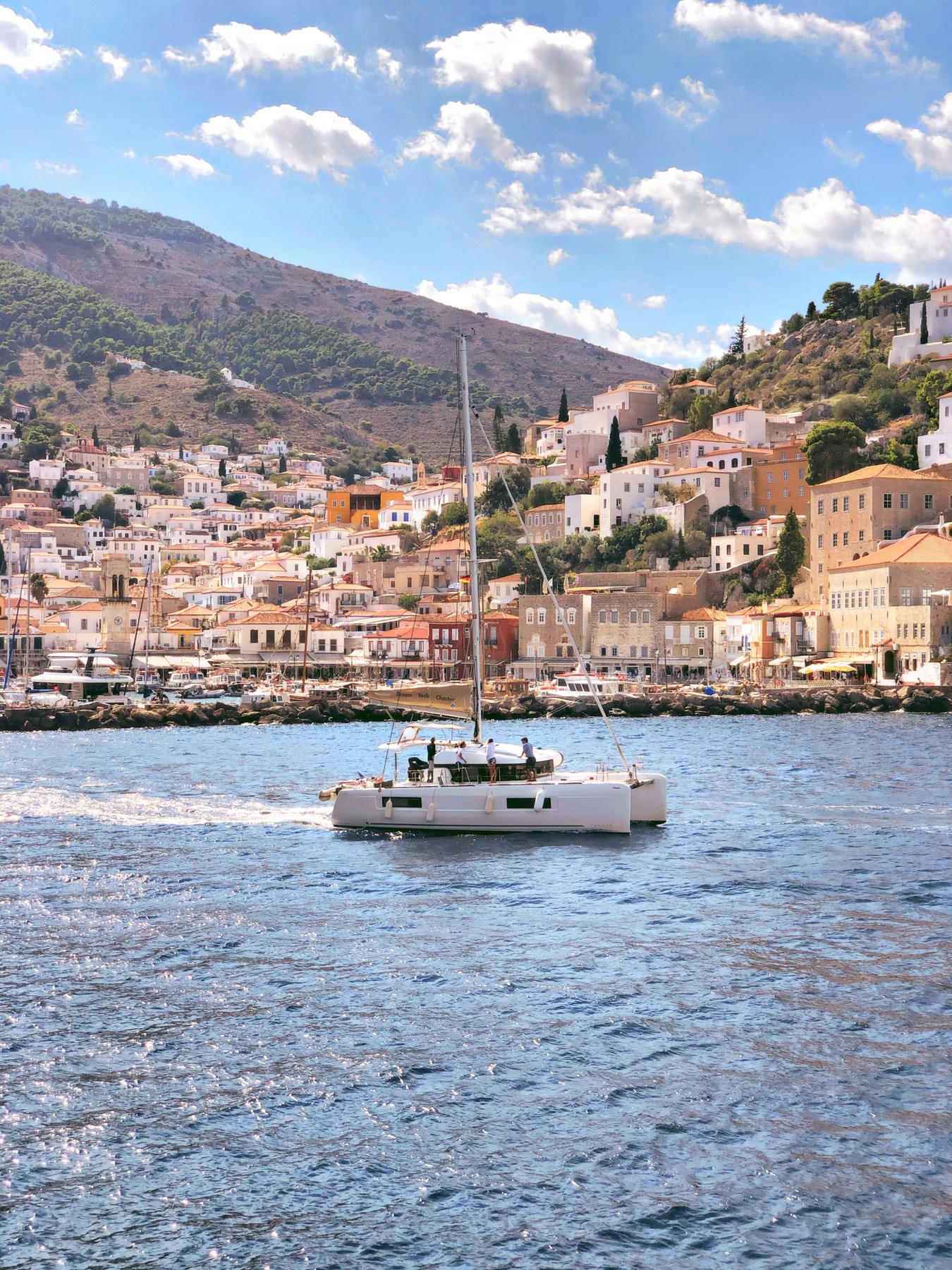 Puerto de Hydra con casas de piedra y barcos de vela, sin autos visibles en el muelle