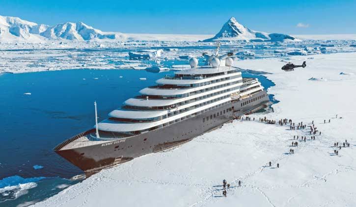 Scenic Eclipse anclado frente a un paisaje glaciar en la Antártida, con helicóptero sobrevolando